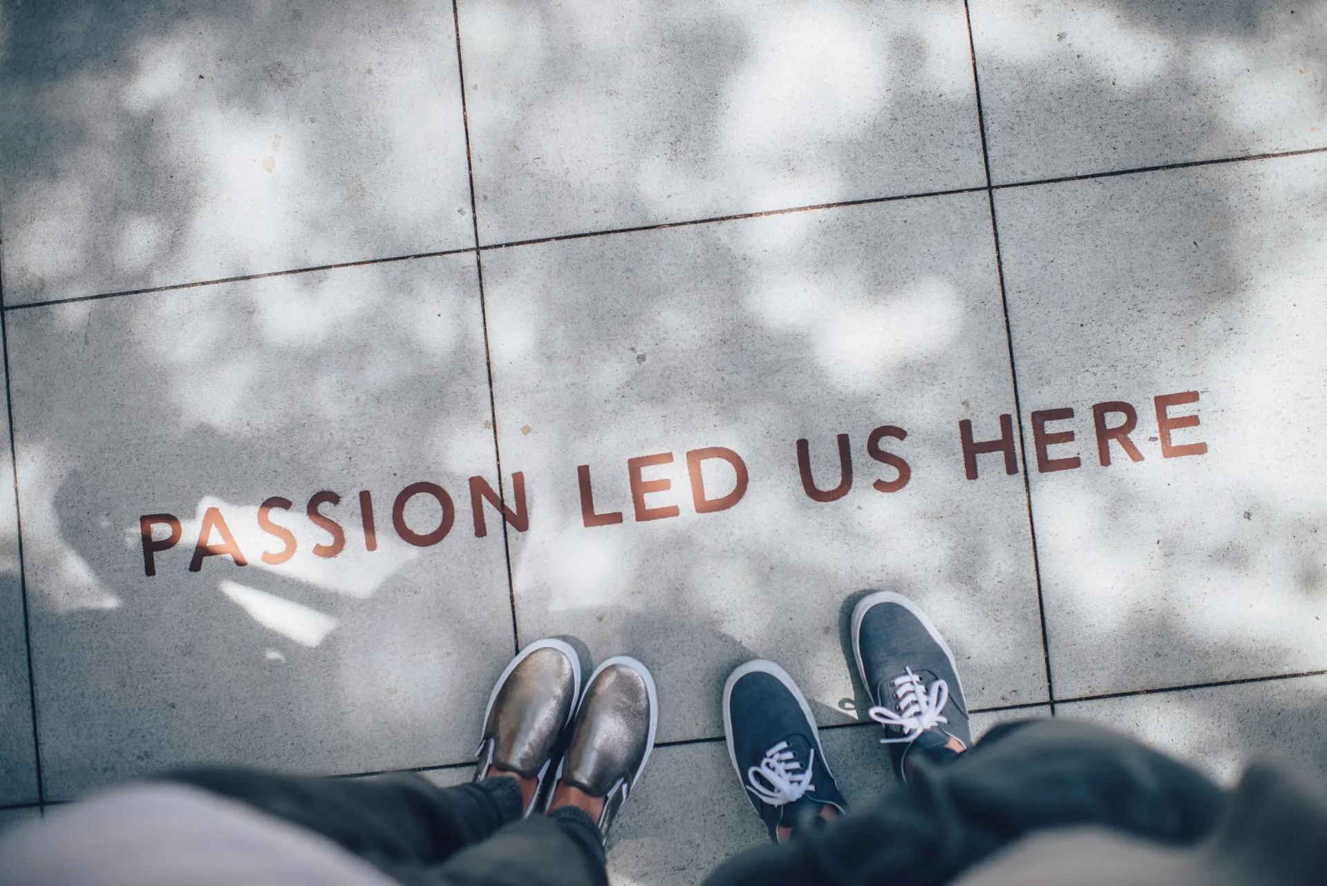 Two pairs of sneakers on a sidewalk stenciled with the words Passion Led Us Here