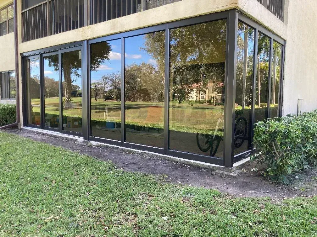 Ground-floor glass patio enclosure with dark aluminum frames, seen from the lawn outside